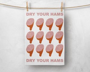 Image of a tea towel pegged with a wooden peg in each top corner, hanging on some twine in front of a concrete looking light grey background. The tea towel has three rows of four hams on it. Across the top and the bottom of the tea towel are the words 'Dry your hams' in a ham coloured pink in all capitals